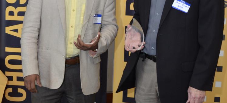 Kevin Sowers and Upal Ghosh holding trophies in front of a black and gold UMBC poster