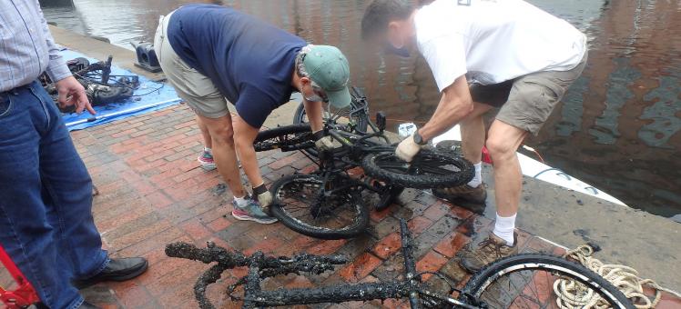 two people inspect two bicycles that were just pulled out of the water