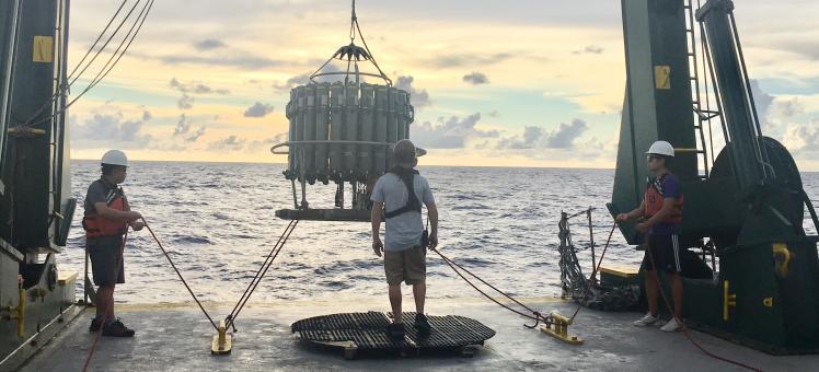 a team of scientists lowers a CTD into the water off of a research boat
