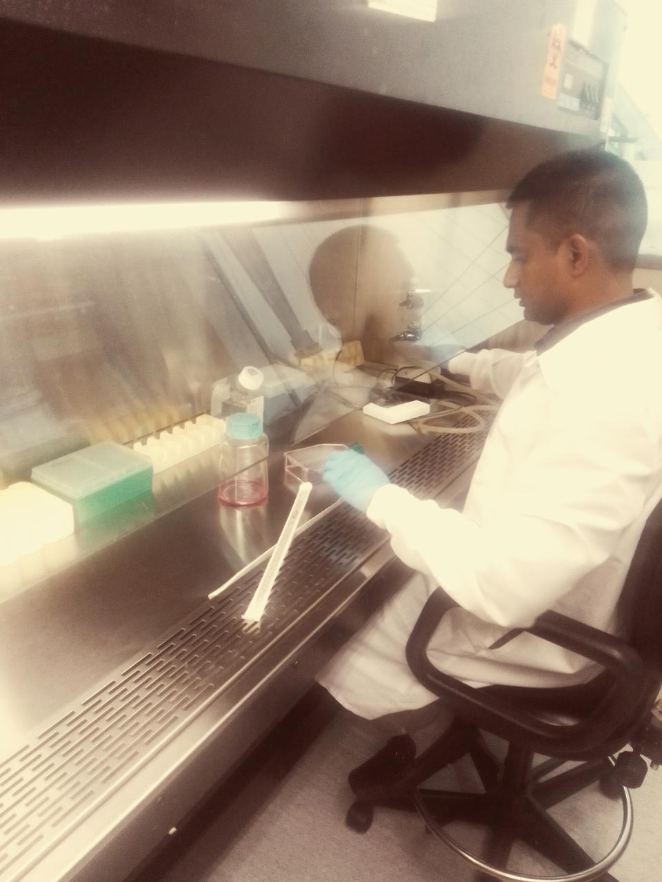 Muddassar Iqbal in a lab coat sits at a fume hood