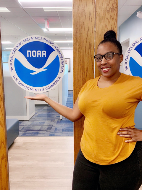 Shadaesha Green poses next to a door with the NOAA logo