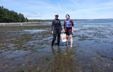 Tori and a labmate hold a bucket in a mud flat