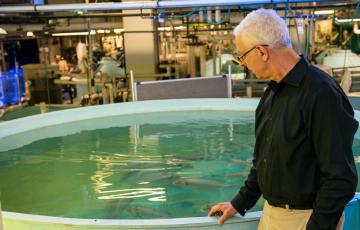 Dr. Zohar stands with his hand on a large round tank of fish