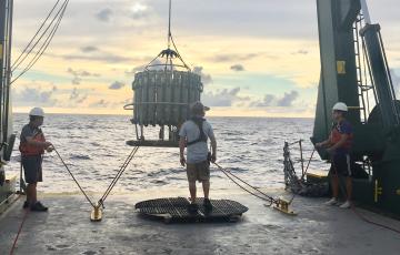 a team of scientists lowers a CTD into the water off of a research boat