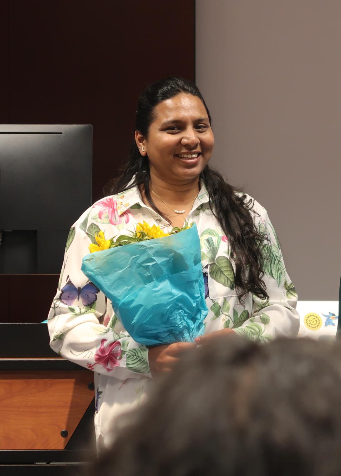 Ronita holding flowers and smiling at the front of a room 